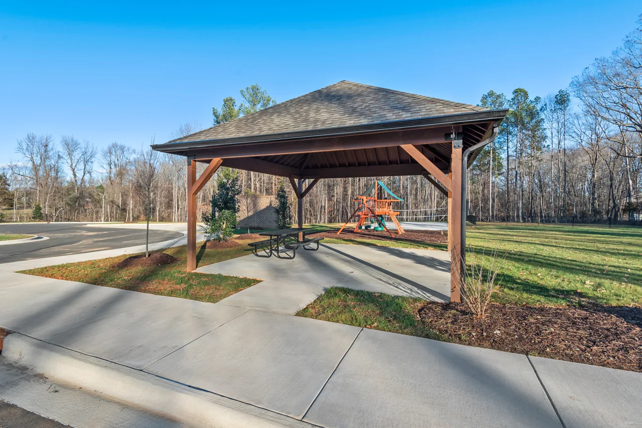 Covered community pavilion with a picnic table and grassy surroundings